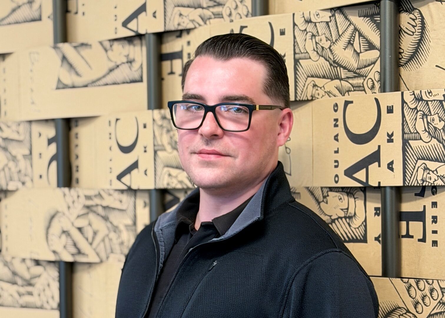 Man with glasses and navy zip up standing in front of branded wall
